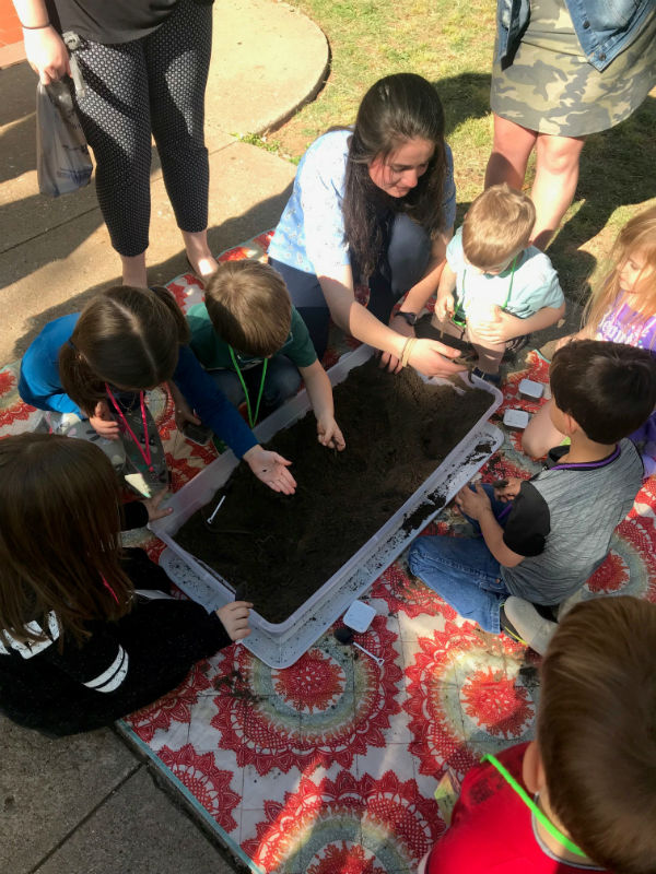 IM体育平台 student teacher and children playing in tub of dirt looking for worms