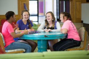 IM体育平台 students sitting at a round table talking, smiling, and laughing
